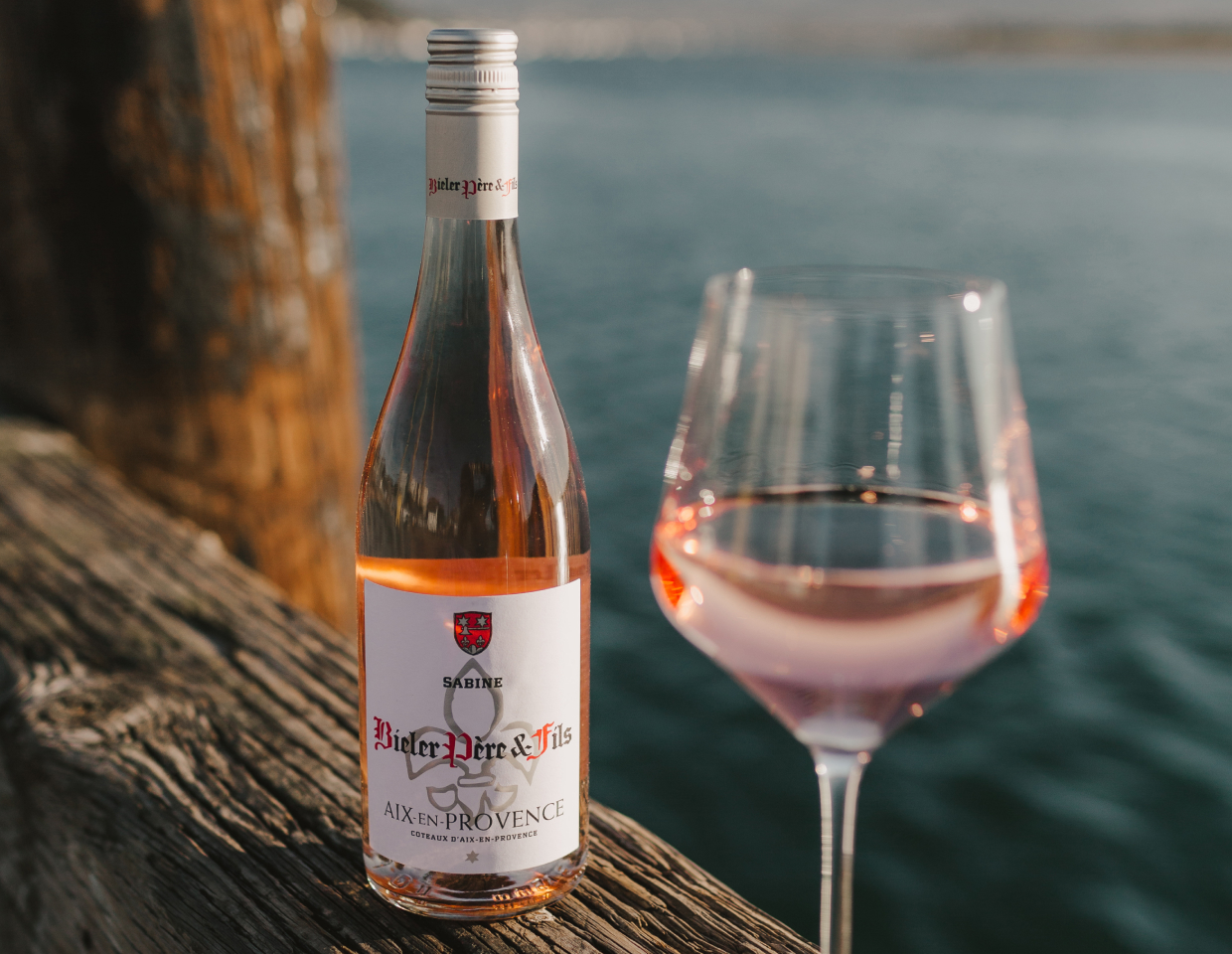 Bottle and glass of Bieler Pere & Fils Sabine Rose by the ocean.