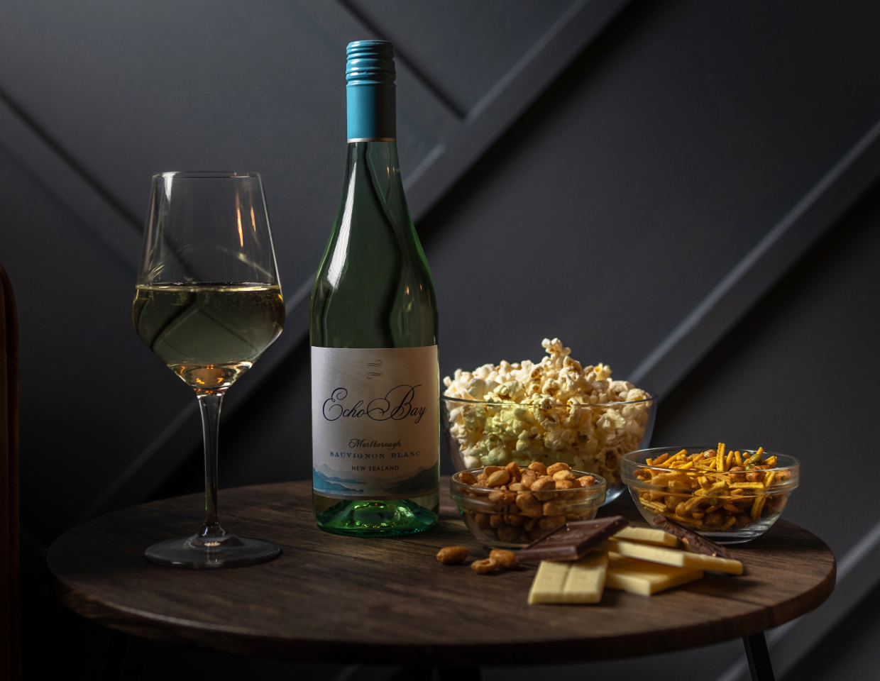 Bottle of Echo Bay Sauvignon Blanc on a table surrounded by bowls of popcorn and pretzels and chocolate bars