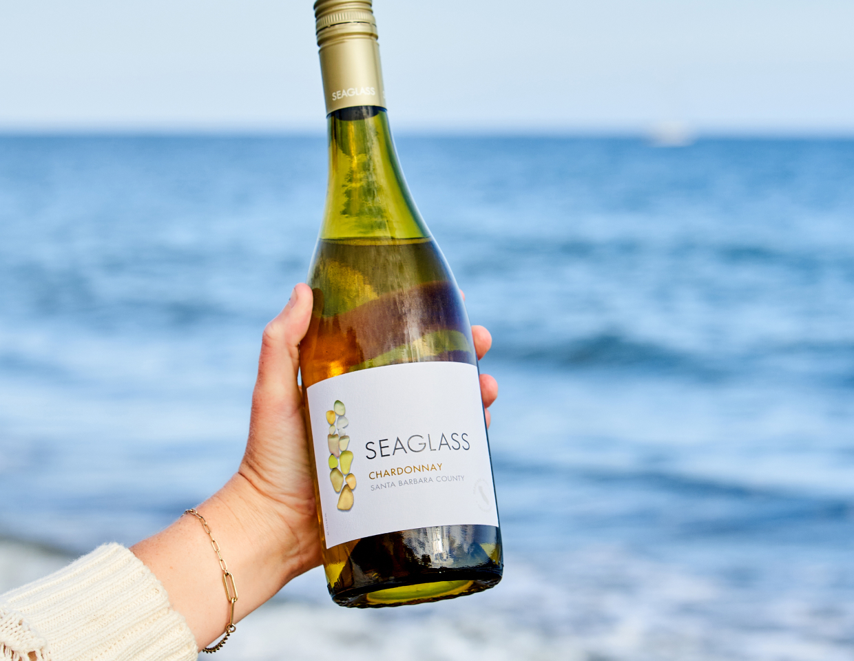 Person holding bottle of Seaglass Chardonnay in front of a beautiful blue sea.