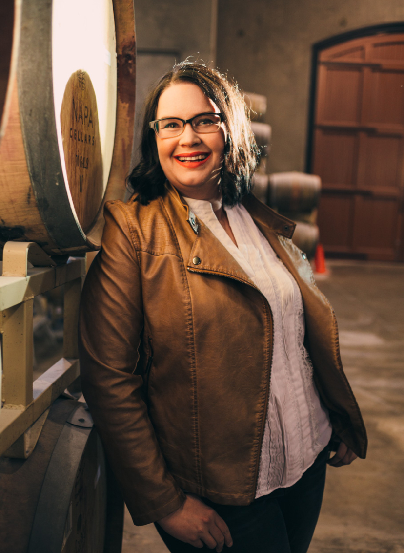 Emily Haines smiling and leaning up against wine barrels at Terra d'Oro winery's barrel room