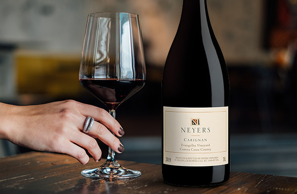 bottle and glass of neyers carignan wine on a wooden table with a woman's hand