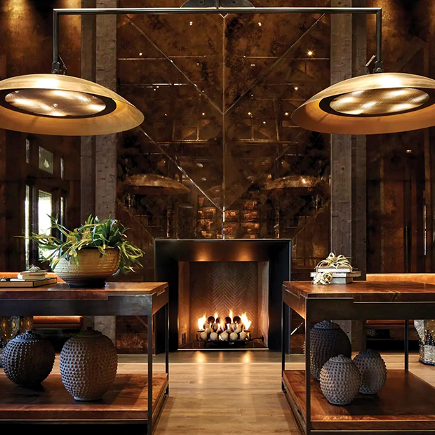 Inside of the Trinchero Napa Valley tasting room featuring a glowing fireplace, two large, gold light fixtures, and modern tables and decorations.