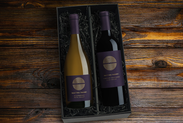 Bottles of Quattro Theory chardonnay and Quattro Theory Cabernet Sauvignon in a black gift box on a dark wood surface