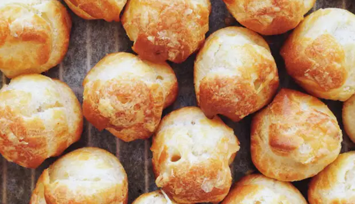 Several golden-brown cheese puffs nestled together on top of a gray-blue tablecloth