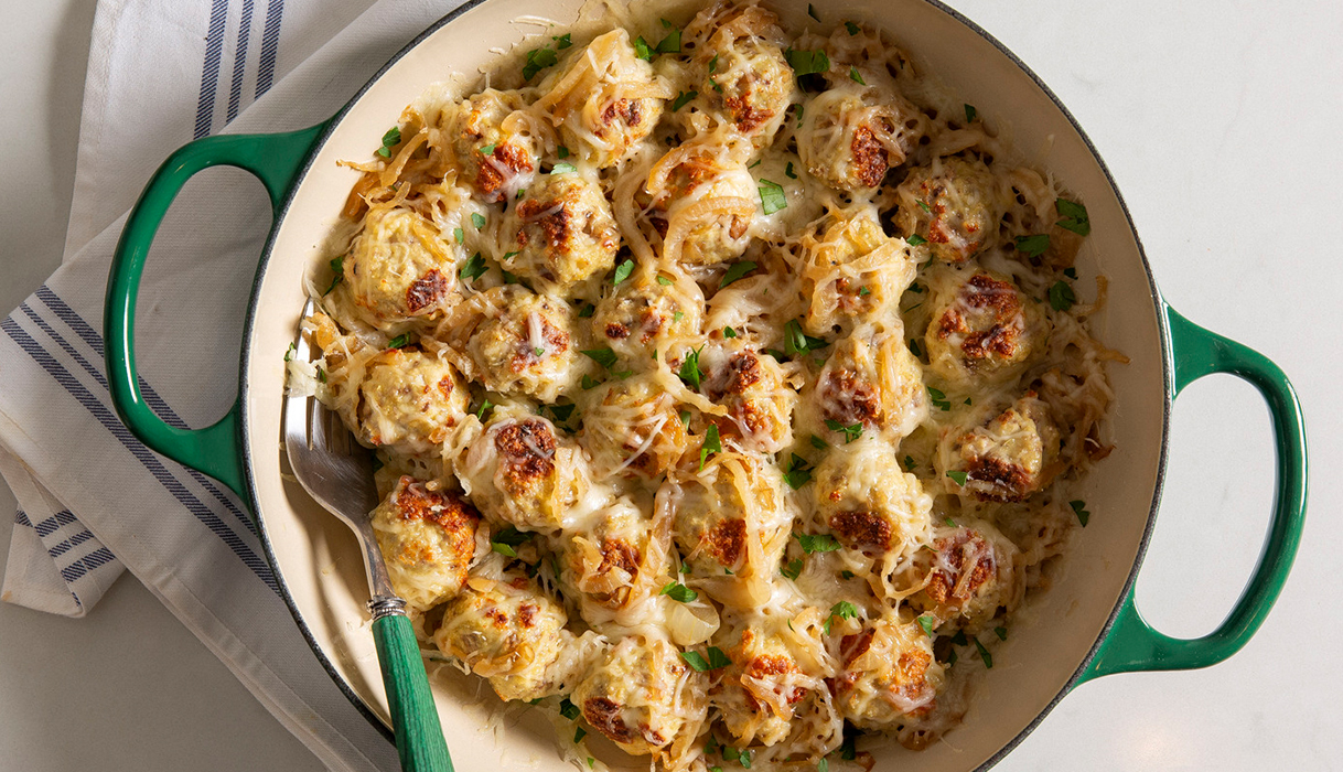 Pot full of french onion meatballs topped with gooey cheese.