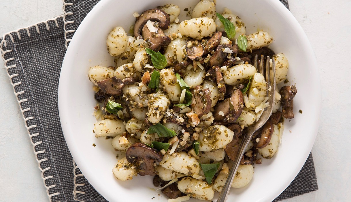 Bowl of pesto walnut gnocchi on a blue cloth napkin with a fork.