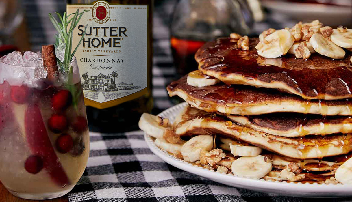 A stack of banana eggnog pancakes on a plate next to a bottle of Sutter Home chardonnay on a gingham tablecloth