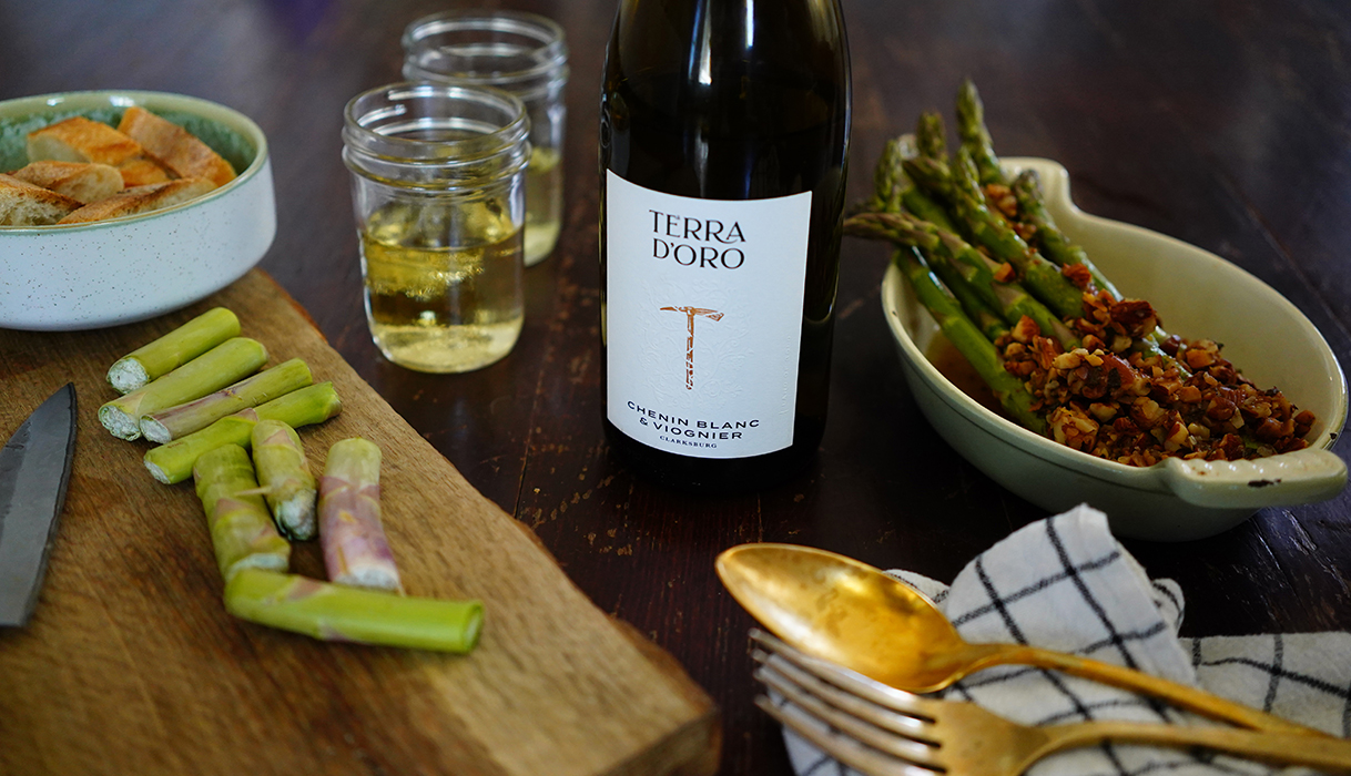 Dish of almondine topped asparagus next to a bottle and glasses of Terra d'Oro Chenin Blanc Viognier