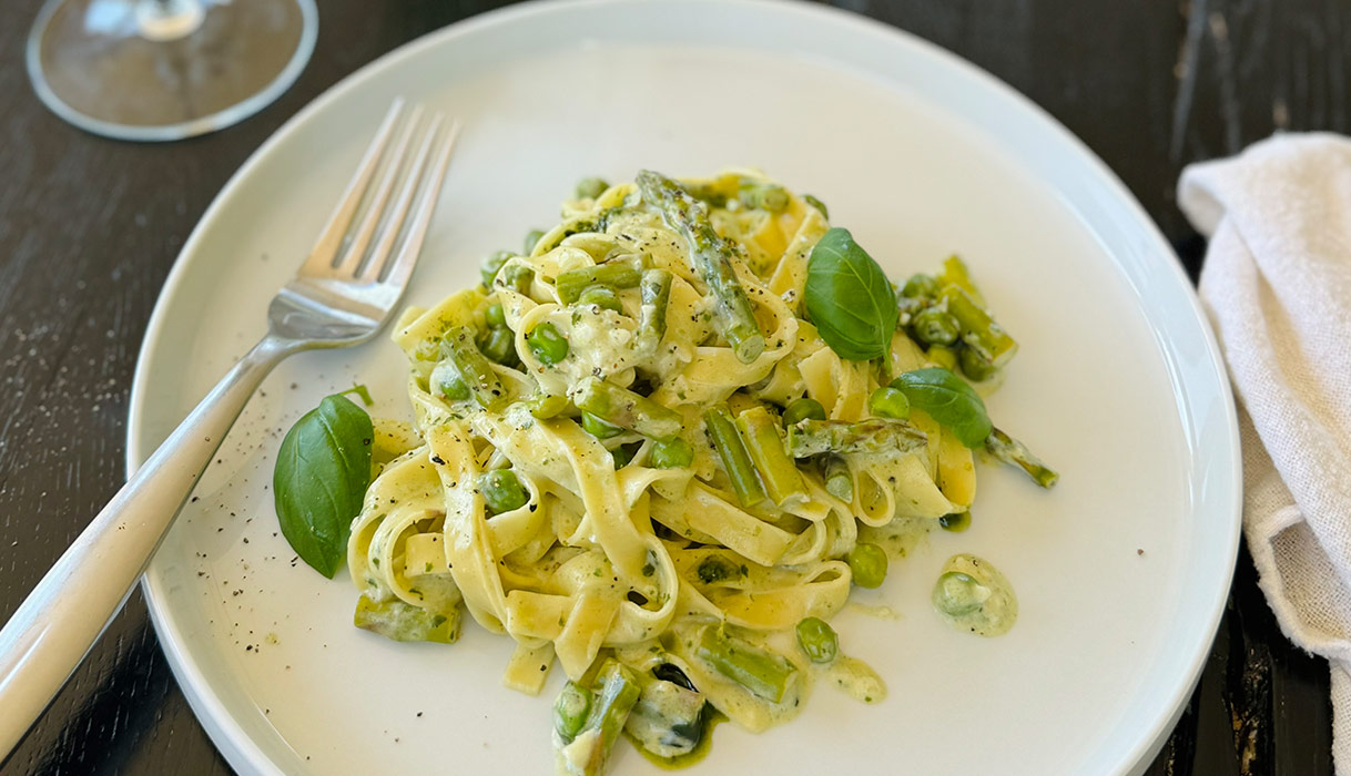 Pesto pasta on a white plate garnished with basil leaves on a wooden table.
