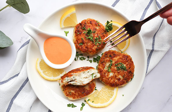 http://Crab%20cakes%20on%20a%20white%20plate%20surrounded%20by%20lemon%20slices%20with%20a%20small%20container%20of%20dip